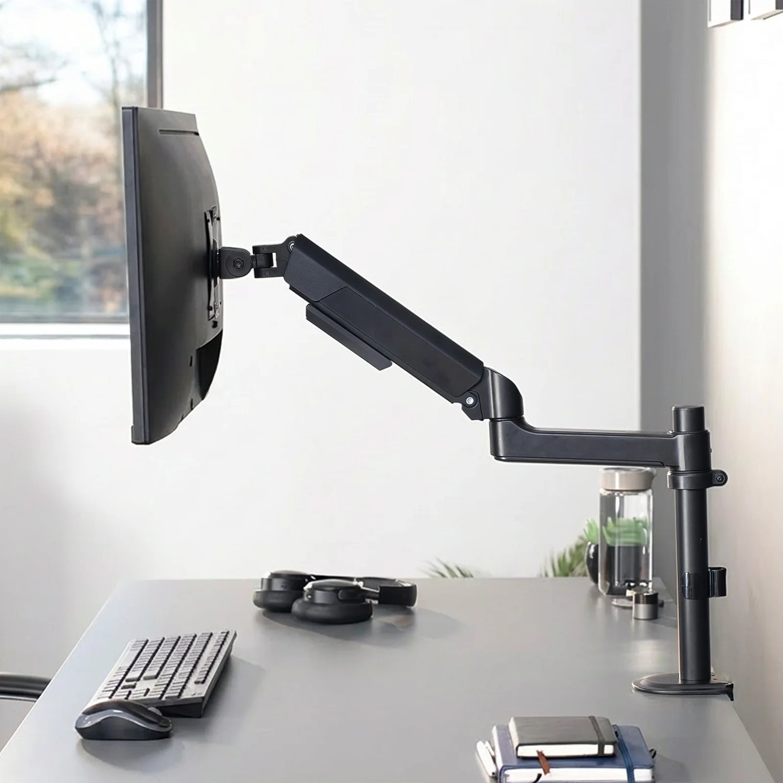 A single monitor floating on an articulating arm above a clear desk, with the keyboard and mouse in the space the stand used to occupy