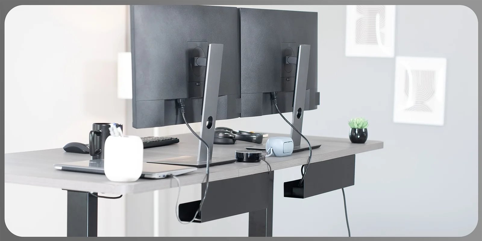 Two steel cable trays screwed under a desk, holding a power strip and the cable slack from two monitors