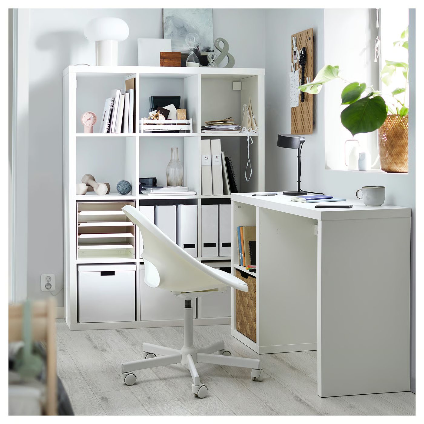 A white IKEA KALLAX desk set against the wall of a small bright room with an office chair pulled up to it