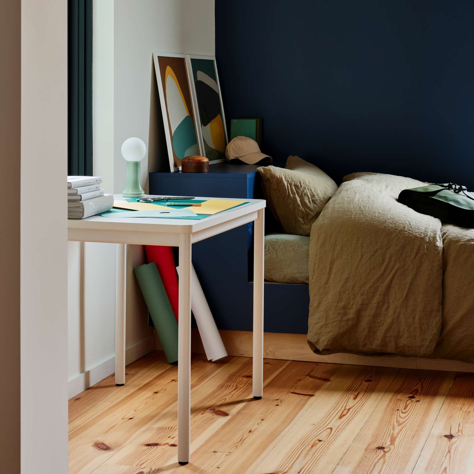 A small white desk in the corner of a bedroom with a bed beside it and a laptop on the worktop