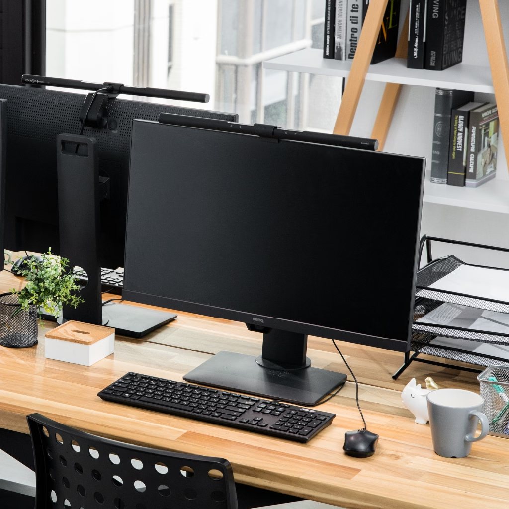 A monitor light bar clipped to the top of a screen, lighting the keyboard and the desk in front of it without standing on the desk