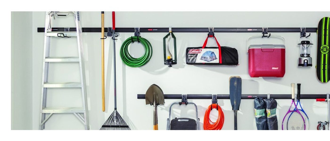A garage wall fitted with a horizontal rail system holding a ladder, rake and hose