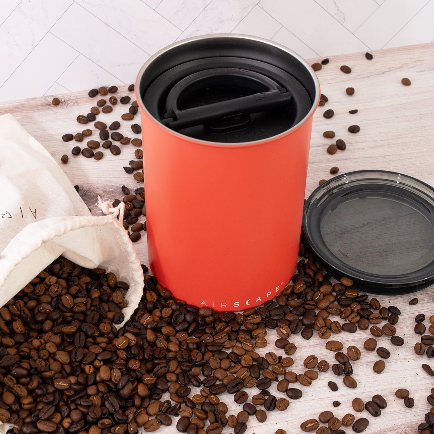 An Airscape coffee canister in coral standing beside a bag of whole coffee beans on a kitchen counter