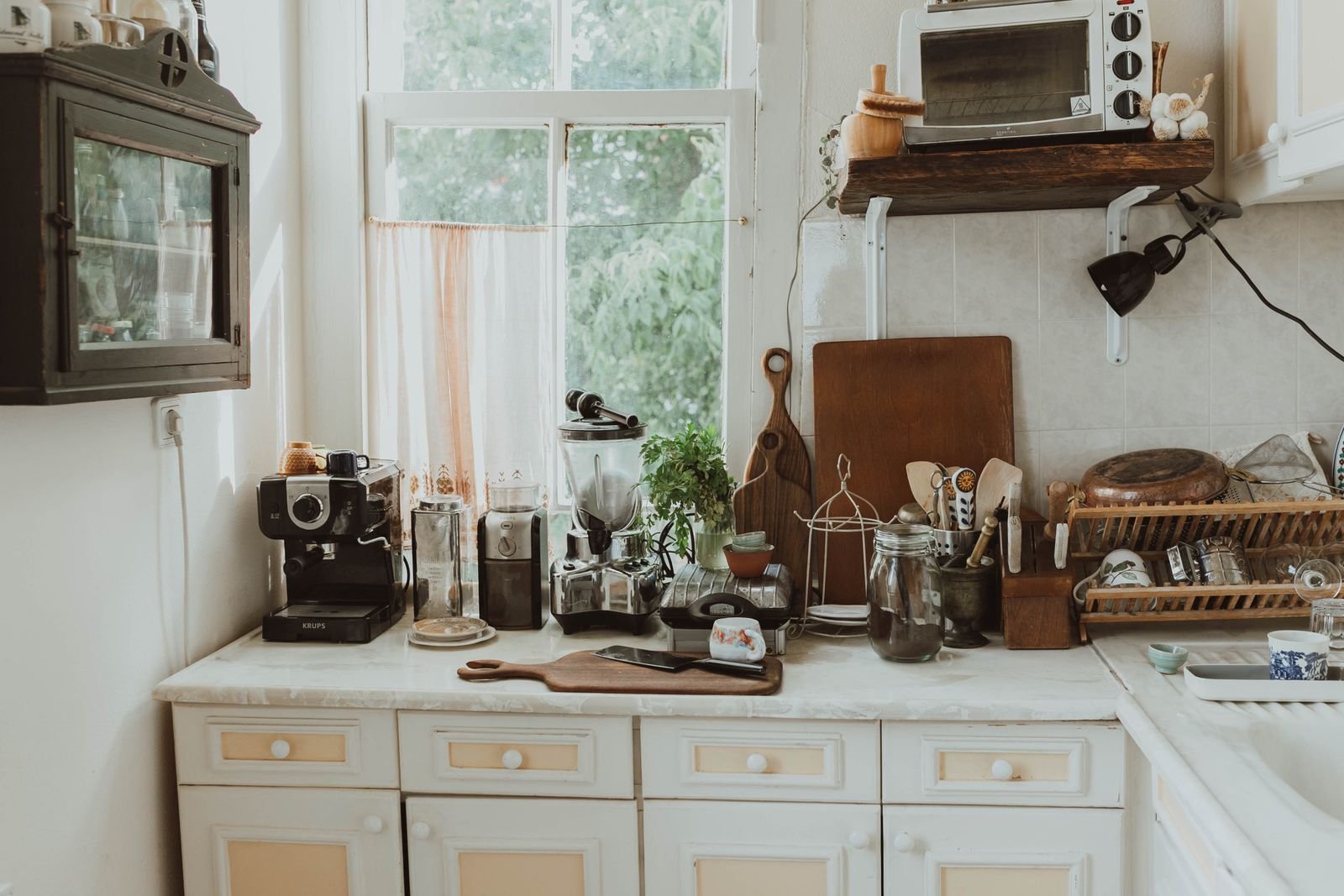 A home coffee corner on a kitchen counter with a shelf mounted above it and daylight from a window