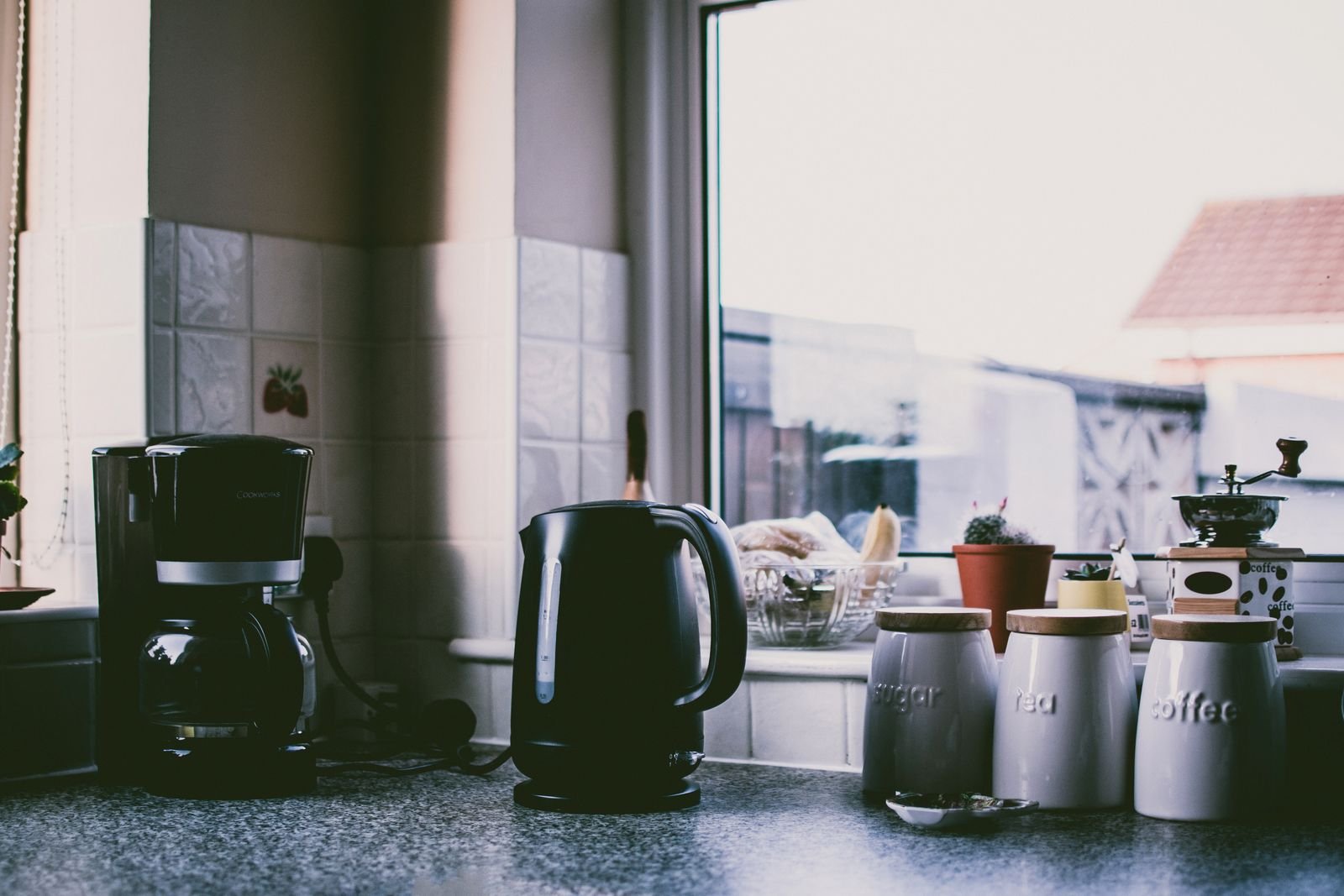 A drip coffee maker and an electric kettle on a narrow kitchen counter below a wall cabinet