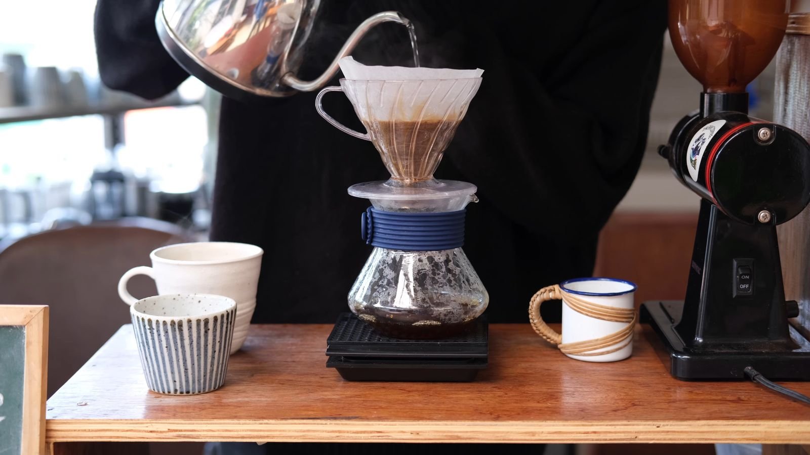 A close-up of water being poured from a gooseneck kettle over a paper filter of ground coffee