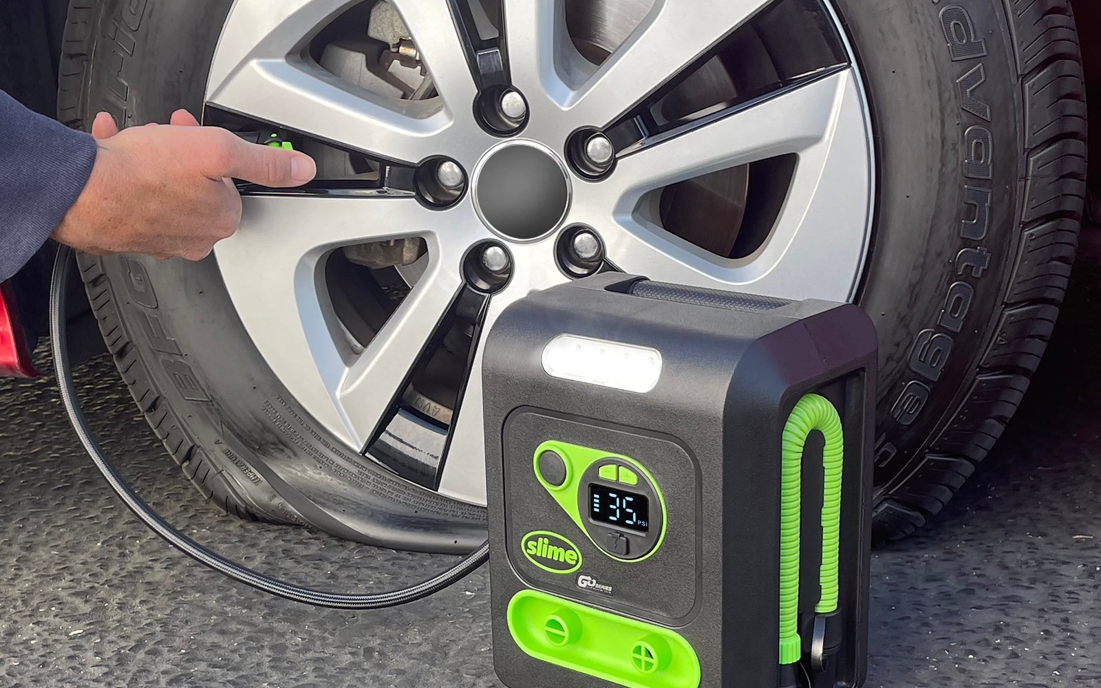 The Slime cordless inflator connected to a car tire valve while a hand holds the chuck on the stem