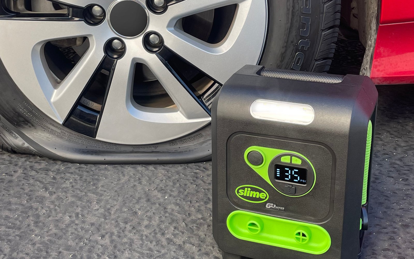 The Slime cordless multi-purpose inflator standing on pavement beside a car wheel, its display reading 35 PSI