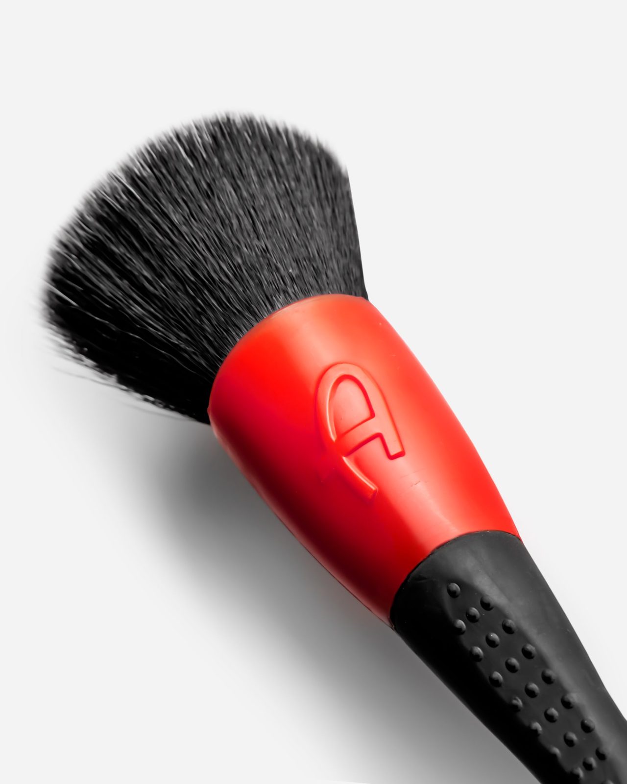 A soft black detailing brush head with a red and black handle photographed close up