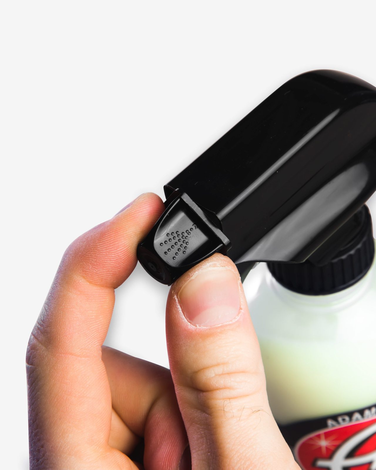 A hand holding a trigger bottle of tire dressing beside a wheel