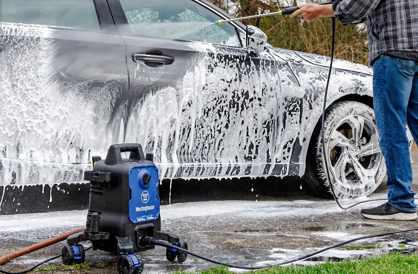 A person foaming a car on a driveway with the Westinghouse ePX3100 electric pressure washer running beside them